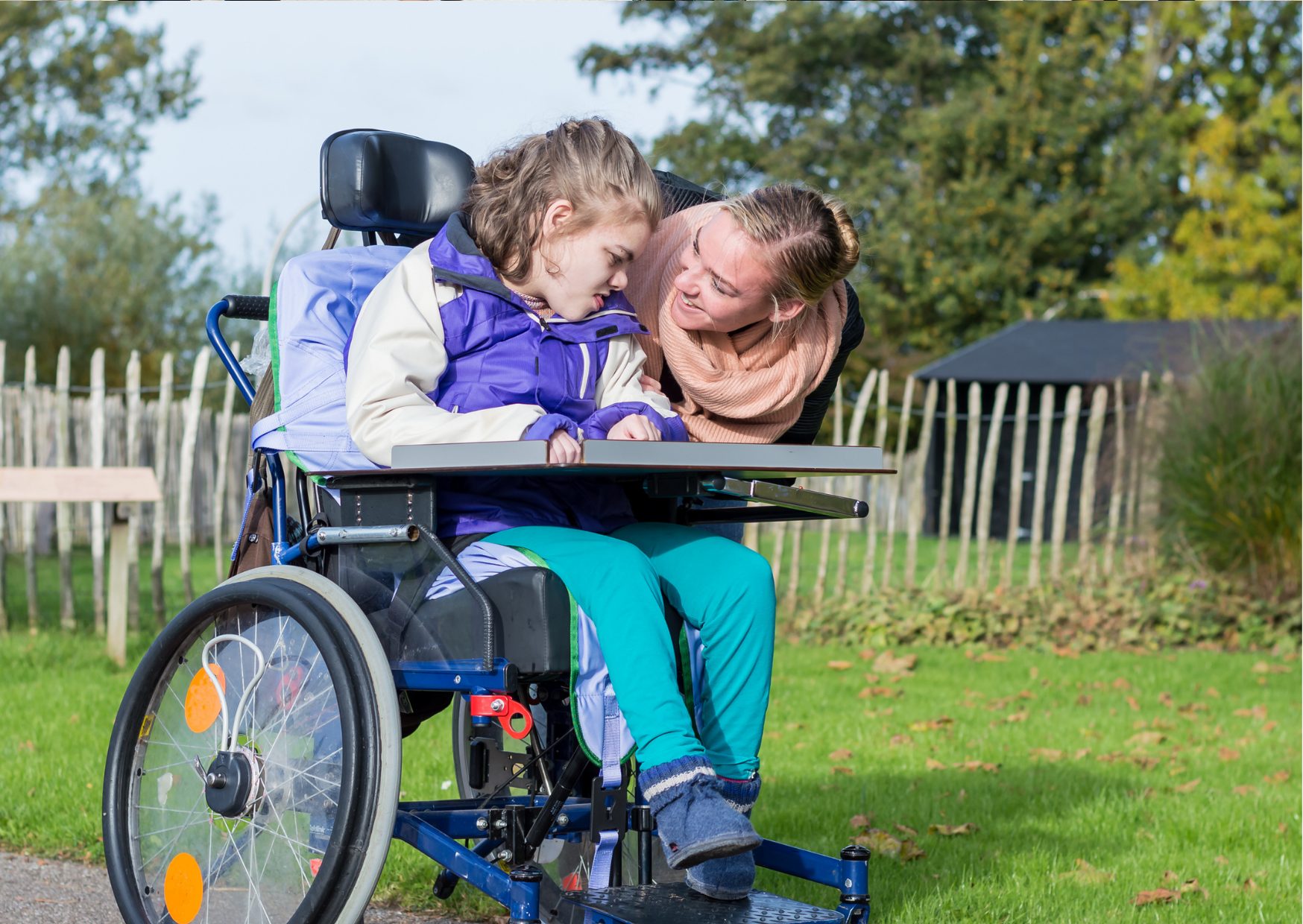 smiling woman bends to talk to a teen girl in a wheelchair