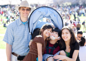 smiling white adult male with three children who are smiling. two girls and one boy. They boy is in a wheelchair.