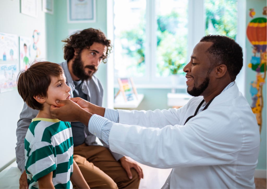 black, male doctor examines young white male while white male dad watches